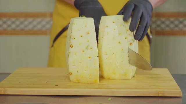 Professional male cook is slicing pineapple on pieces, close-up