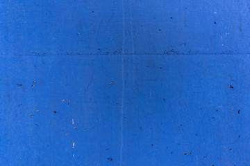 Blue painted concrete wall of a retaining wall in an industrial building, with cracks and air holes
