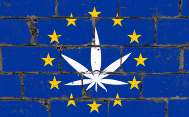 Graffiti street art spray drawing on stencil. Cannabis leaf on brick wall with flag European Union