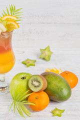 Summer cocktail with various tropical fruits around. Apple, kiwi, tangerine, orange, mango, carambola.
