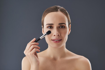 Obraz premium Gorgeous lady holding makeup brush near face and looking at camera