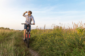 Young man on bicycle in nature in sunlight. Field with flowers, summer landscape with copyspace