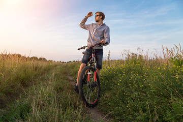 Young man on bicycle, cyclist in field with green grass and flowers, beautiful nature landscape, copy space