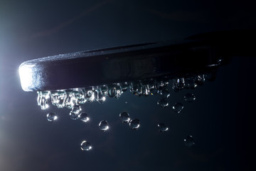 Modern shower with stream drops of water and sunlight bokeh close-up macro on a dark background