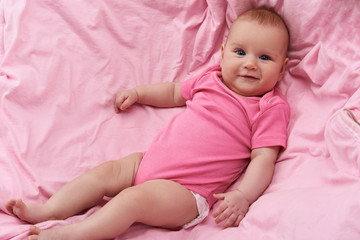 Good-looking baby in pink body wear looking at camera