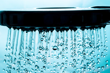 Fototapeta na wymiar Modern shower with stream drops of water and sunlight bokeh close-up macro on a blue background