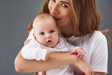 Charming mama looking at camera and kissing her baby