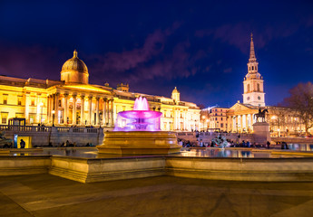 Cityscape view of the famous Trafalgar square of London in evening lights, with colorful fountains...