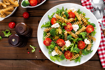 Italian pasta salad with wholegrain fusilli, fresh tomato, cheese, lettuce and broccoli on wooden...