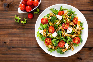 Italian pasta salad with wholegrain fusilli, fresh tomato, cheese, lettuce and broccoli on wooden rustic background. Mediterranean cuisine. Cooking lunch. Healthy diet food. Top view