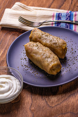 cabbage rolls stuffed with ground beef and rice served on a white plate on an old rustic table with sour cream in a bowl, view from above, close-up, flatlay