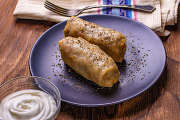 cabbage rolls stuffed with ground beef and rice served on a white plate on an old rustic table with sour cream in a bowl, view from above, close-up, flatlay