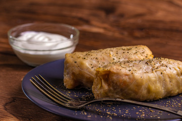 cabbage rolls stuffed with ground beef and rice served on a white plate on an old rustic table with sour cream in a bowl, view from above, close-up, flatlay
