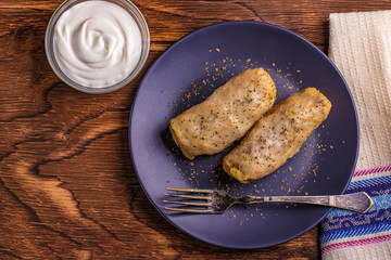 cabbage rolls stuffed with ground beef and rice served on a white plate on an old rustic table with sour cream in a bowl, view from above, close-up, flatlay