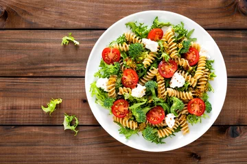 Poster Italian pasta salad with wholegrain fusilli, fresh tomato, cheese, lettuce and broccoli on wooden rustic background. Mediterranean cuisine. Cooking lunch. Healthy diet food. Top view © Sea Wave