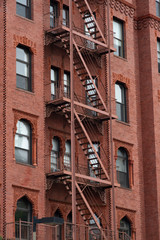 Fototapeta na wymiar Fire escape stairs-downtown back alley architecture-steel and red brick background