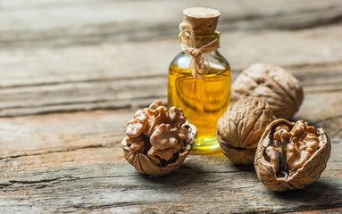 Walnut oil in glass of bottle, whole big peeled walnut kernel with thin shell on wooden background....