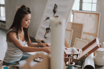 Cheerful lady smiling wheil working at the table in art studio