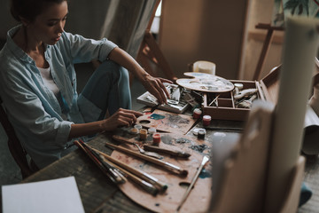 Concentrated female artist taking paints and holding spatula
