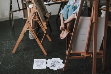 Naklejka premium Barefooted woman sitting on the chair and her drawings lying on the floor