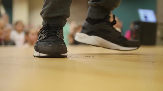 People on the open lesson indoors. The dancer makes a movement with his feet.