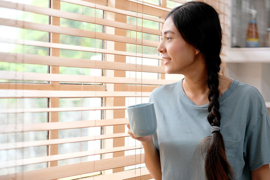 Young asian woman holding a coffee cup while standing in kitchen at home background, people lifestyle