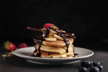 Pancakes with strawberries, raspberries, banana, chocolate, pistachios and cream on a white plate. Horizontal. Copyspace