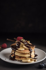 Pancakes with strawberries, raspberries, banana, chocolate, pistachios and cream on a white plate. Vertical. Copyspace
