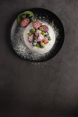 Homemade Pavlova meringue cake with blueberries, strawberries, raspberries, kiwi and powder sugar. Vertical. Copyspace. Top view