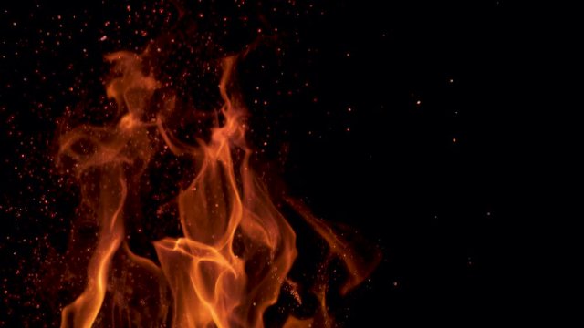 SLOW MOTION, MACRO: Cinematic shot of flames flickering in the darkness of the night. Colorful flames flickering and sparkles flying out of a campfire in pitch black wilderness. Orange fire blazing.