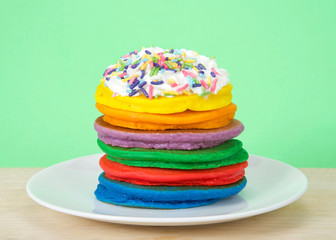 Stack of bright colorful pancakes topped with whipped cream and candy sprinkles with green background. Fairy pancakes for National International Pancake day.