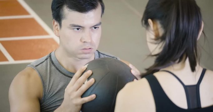 Close up shot of Young caucasian man doing sit-ups with a ball next to his personal trainer in fitness hall. 