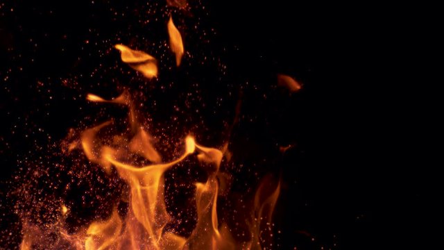 SLOW MOTION, MACRO: Colorful flames flickering and sparks come flying out of a bonfire in the pitch black nature. Orange fire blazing and spitting out glowing particles. Cinematic shot of flames.