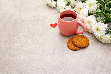 Romantic breakfast concept. A cup of black tea, oatmeal cookies, bouquet of chrysanthemums. For Valentine's Day or March 8, on a stone background