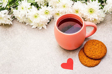 Romantic breakfast concept. A cup of black tea, oatmeal cookies, bouquet of chrysanthemums. For Valentine's Day or March 8, on a stone background