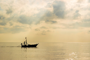 Obraz premium Silhouetted photograph showing a fisher man sailing a small fishing boat in the sea close up.