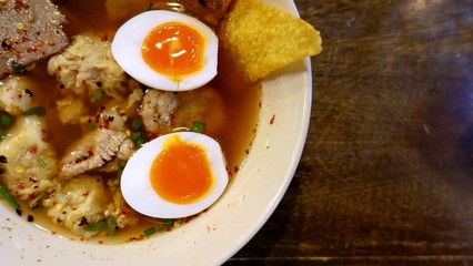 Thai style noodle with Tom Yum soup top with soft boiled egg, minced pork annd roasted chili and peanut on the wooden table, food photography concept dark color  tone