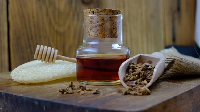 A bottle of propolis tincture and a wooden scoop of propolis granules. Medical preparations bee propolis. Bee glue. Apitherapy. How to treat bee products.