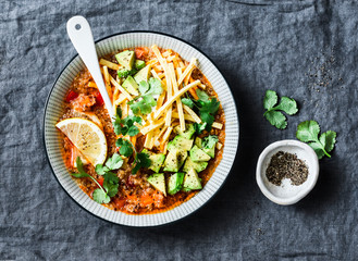 Crock pot vegetarian quinoa tomato soup with corn tortilla chips, avocado and cilantro on grey background, top view