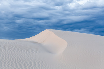 Fototapeta na wymiar Beautiful sand ripples in white dune peak under stormy skies