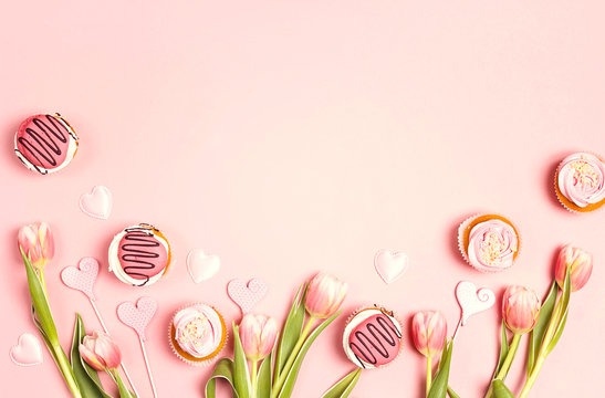 Tasty cupcakes with tulips on pink pastel background. St. Valentine, Mothers, Womens Day concept. Copy space, overhead shot.