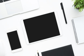 White tablet and smartphone with empty blank screens are on top of white office desk table. Top view, flat lay.