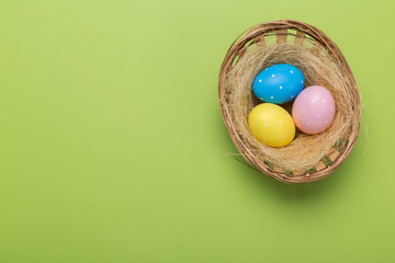 Colorfull easter eggs in nest on green pastel color background with space.