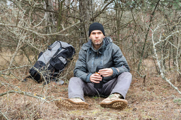 hiker man resting in the forest and drinking tea from the thermos
