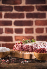 Raw beef ribe-eye steak with salt pepper and herbs on wooden butcher board