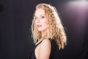 Naklejka premium Fashion and model concept - Portrait of beautiful young sexy blond woman in a black dress posing against a white wall with copy space