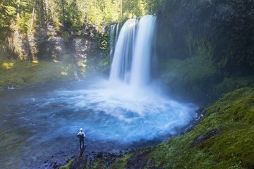 Woman standing by a Koosah Falls, also known as Middle Falls, is second of the three major waterfalls of the McKenzie River, in the heart of the Willamette National Forest, in USA state of Oregon. 