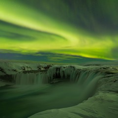 A stunning aurora above the landscape of Godafoss waterfall in winter Iceland. Green northern lights. Starry sky with polar lights. Green northern lights background