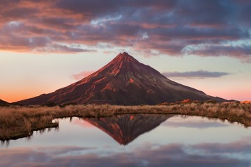 Mount Taranaki under the blue sky with grass as a foreground in the Egmont National Park, the most...