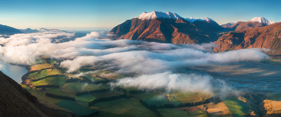 The valley is flooded in mist in a mountain environment. Over the fogs, only the high peaks of the mountains rise beneath the sunny sky. Misty morning on the Southern Island New Zealand, Christchurch - obrazy, fototapety, plakaty